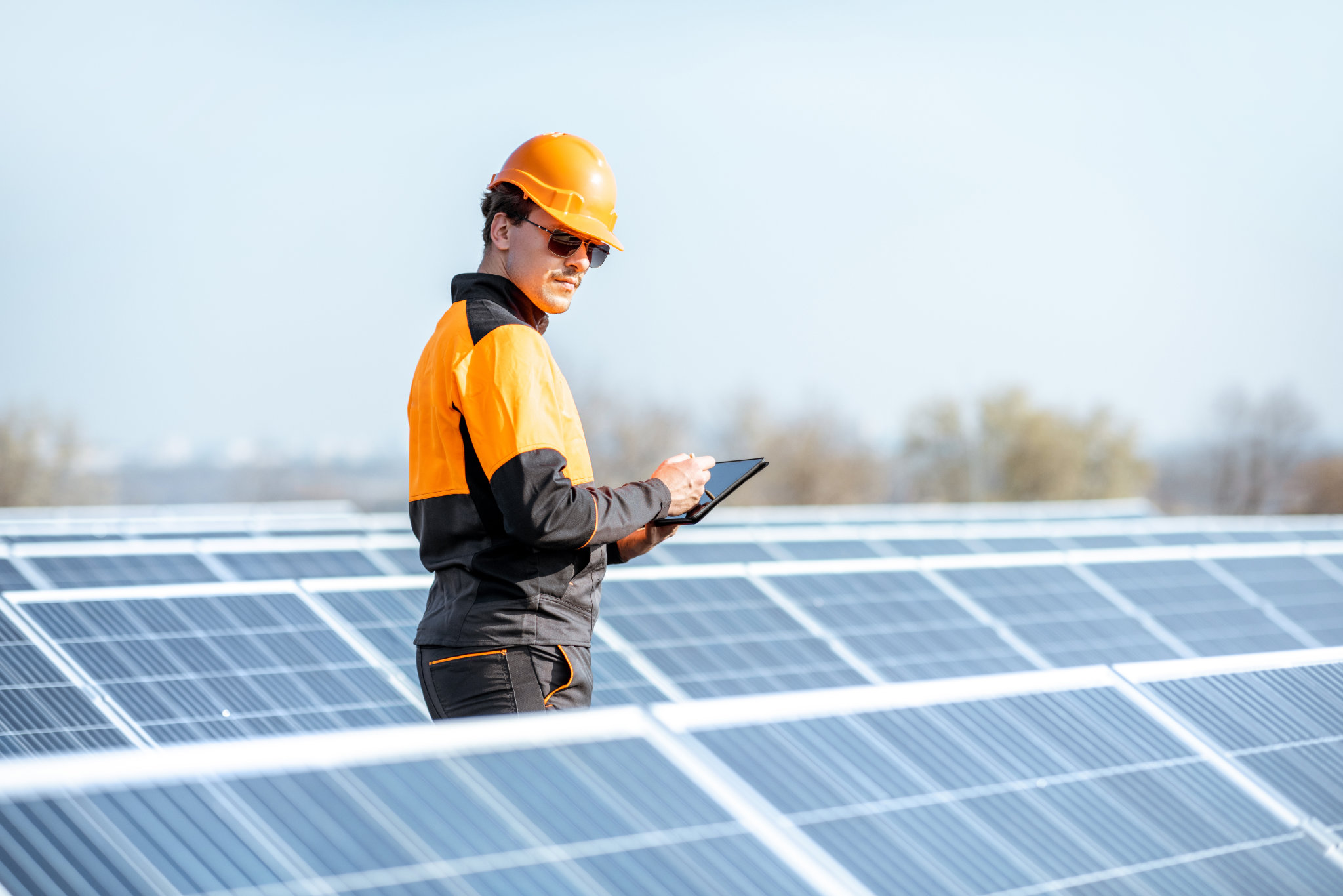 Ingeniero en ropa de trabajo de protección realizando servicio de paneles solares con tableta digital en planta fotovoltaica de azotea. Concepto de mantenimiento y configuración de la estación de energía solar.